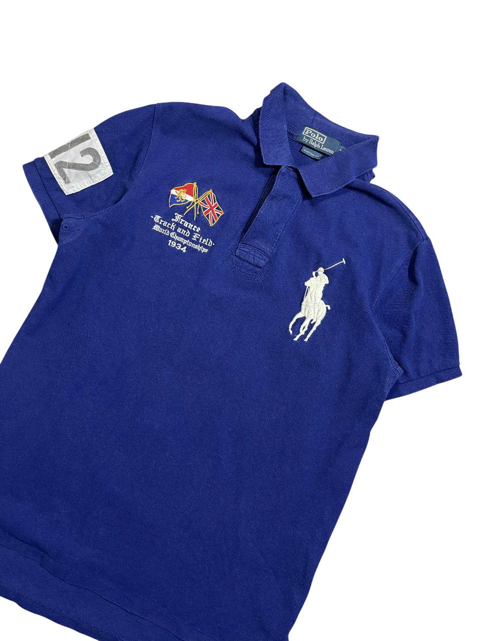 Kék vintage Ralph Lauren póló, hímzett logóval és zászlókkal, sportos streetwear stílus